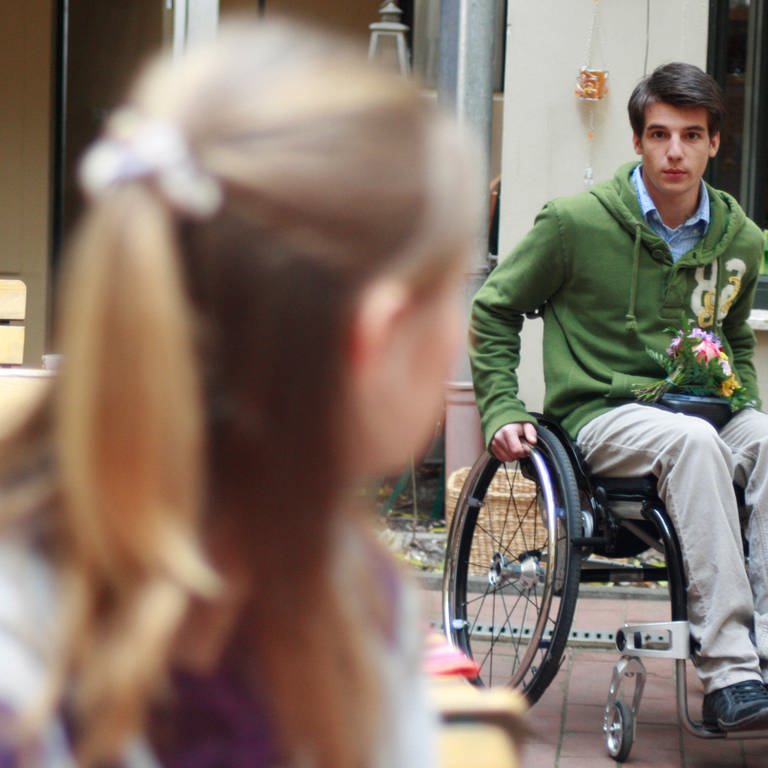 Peter kommt mit seinem Rollstuhl in den Innenhof einer Gaststätte.