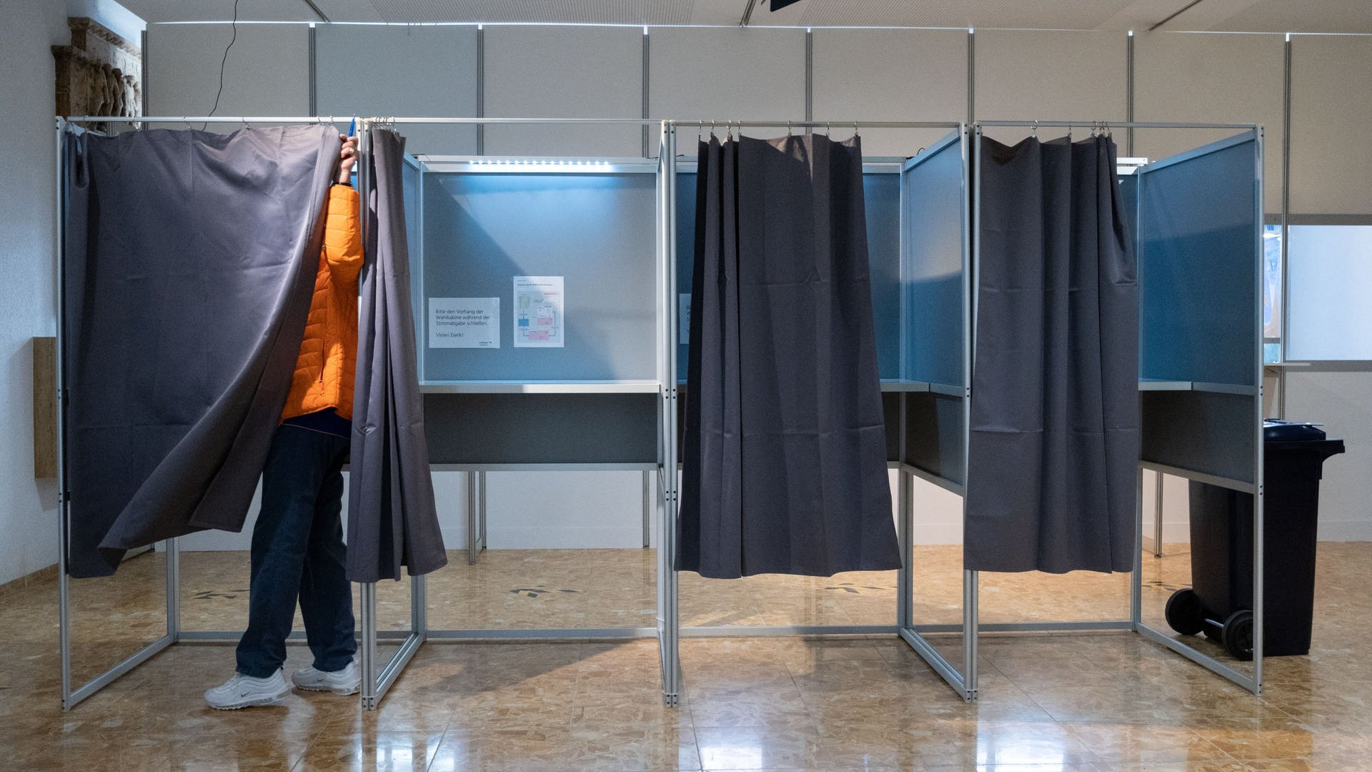 Ein Briefwähler schließt im Rathaus den Vorhang seiner Wahlkabine.