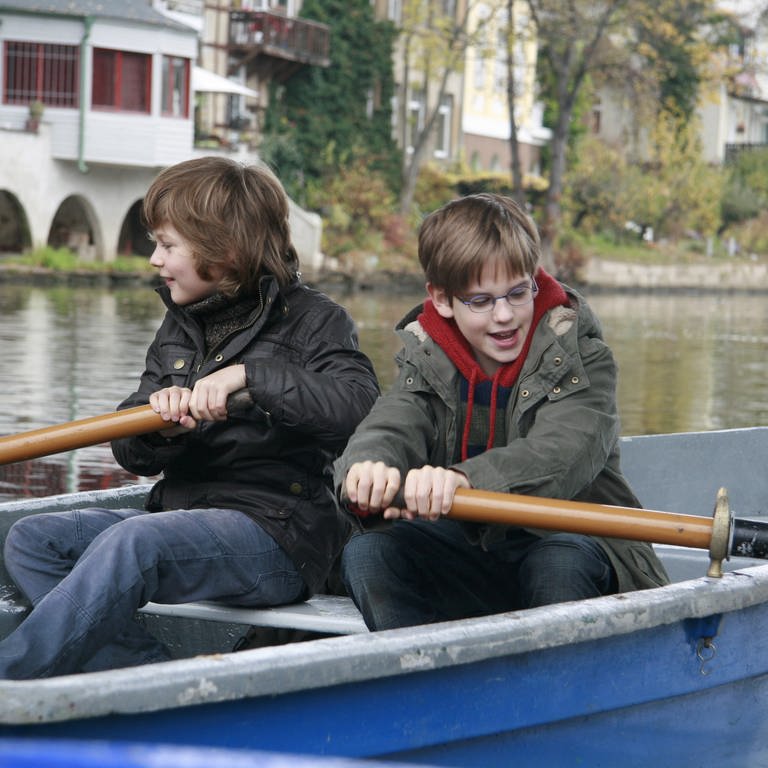 Moritz und Justin sitzen in einem Ruderboot und paddeln.