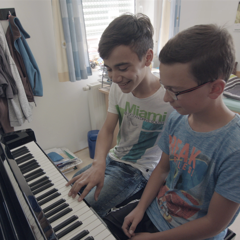 Anwar sitzt mit einem Freund am Klavier und lernt Klavierspielen (Foto: SWR)