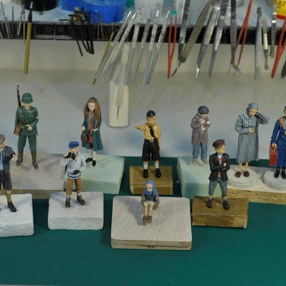 Alle Puppen der Puppenwelt auf kleinen Holzklötzen, im Hintergrund Werkzeug.  (Foto: LOOKSfilm/Momakin)