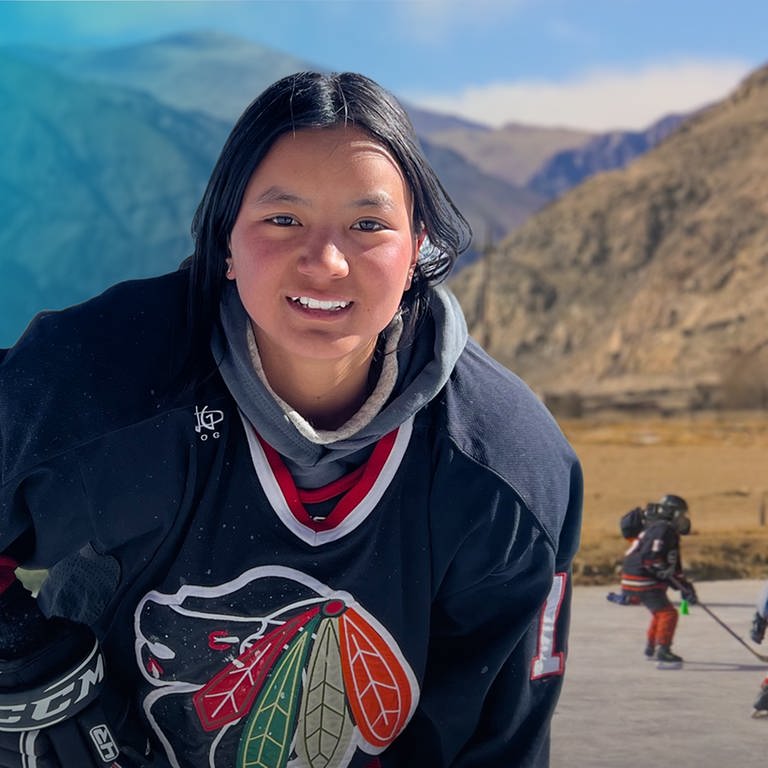 Mädchen spielt Eishockey vor Bergkulisse