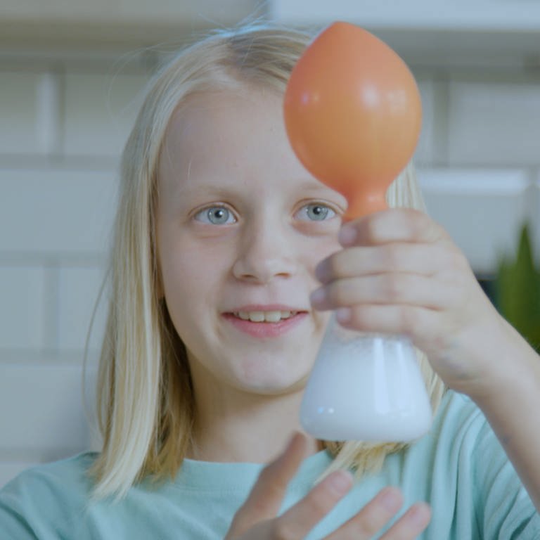 Ida bläst einen Luftballon mit Sprudelwasser und Brausepulver auf