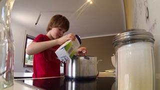Nik schüttet Milch in einen Topf um Milchreis zu kochen. (Foto: SWR)