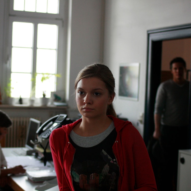 Linda im Sekretariat der Direktion, im Hintergund kommt Lehrer Lammers zur Tür hinein. (Foto: SWR, MDR)