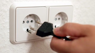 Jeman zieht den Stecker eines Gerätes aus einer Steckdose