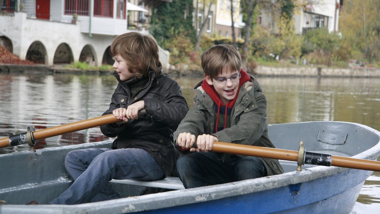 Moritz und Justin sitzen in einem Ruderboot und paddeln.