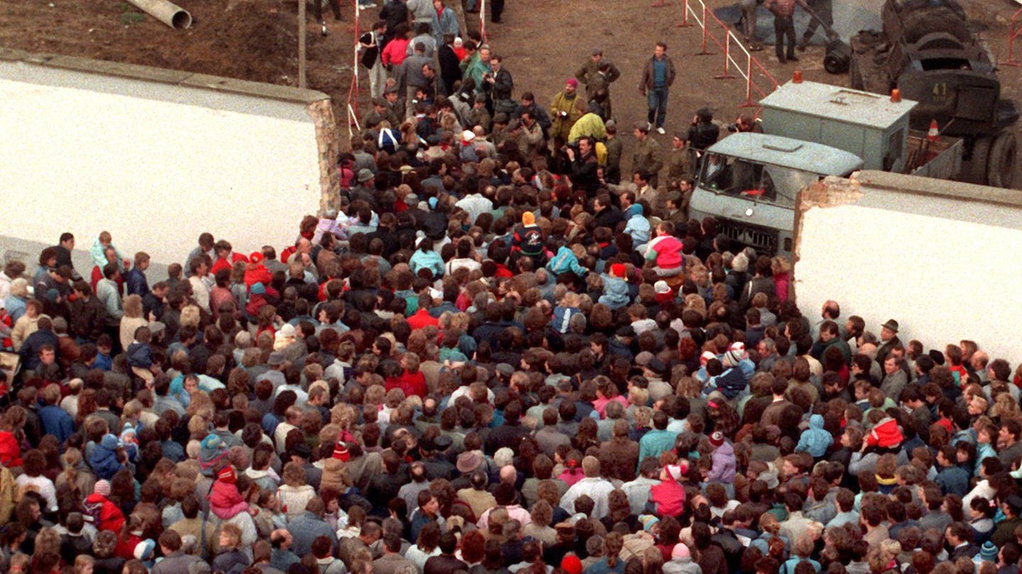 Menschenmenge drängt durch Öffnung in der Mauer